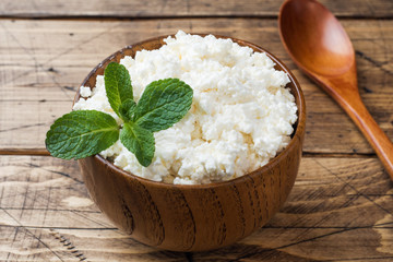 Homemade cottage cheese with mint in a bowl on old wooden table.
