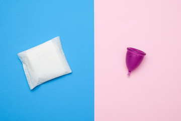 Different types of feminine hygiene products - menstrual cup, sanitary pads on blue and pink background. Selective focus