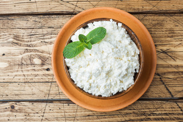 Homemade cottage cheese with mint in a bowl on old wooden table. Copy space