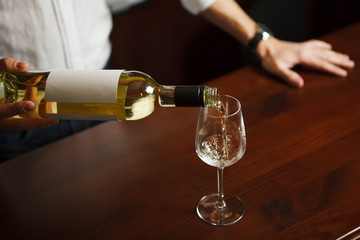 Male sommelier pouring white wine into long-stemmed wineglasses.
