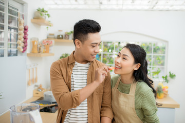 Beautiful happy asian couple are feeding each other in the kitchen.