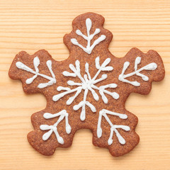 Macro shot of decorated Christmas gingerbread snowflake biscuit on wooden background