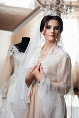 Morning of beautiful bride near the wedding dress. Beauty, fashion. Bride in a white robe plays with her veil. Bride hairstyle, bride dress up at home in a robe. Nice cute girl in a boudoir robe stand