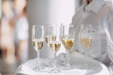 A waiter in a white shirt holds glasses of champagne on the tray
