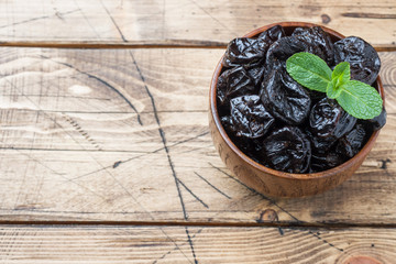Bowl with tasty dried plums on wooden table Copy space