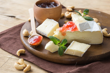 Cutted brie or camembert cheese on gray wooden background with nuts, cherry jam. Italian food concept.