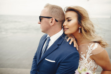 Beautiful bride in a long white dress. Handsome fiance in a blue suit. Couple near ocean