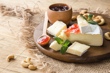 Cutted brie or camembert cheese on gray wooden background with nuts, cherry jam. Italian food...