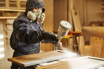Close-up portrait of worker using spray gun and painting wood.