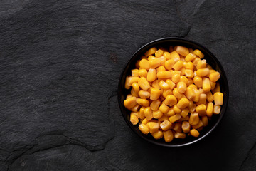 Canned sweet corn in a black ceramic bowl isolated on black slate. Top view. Space for text.