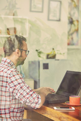 Modern bearded man using cellphone and drinking coffee with laptop.