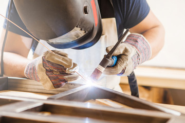Male in face mask welds with argon-arc welding