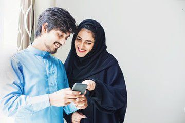 Happy young muslim couple using app on mobile phone at home