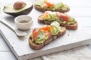 sandwich with avocado and salmon on a light background, green onions and gluten-free grain bread, radishes and tomatoes. concept diet food, copy space, sandwich take away, healthy fast food