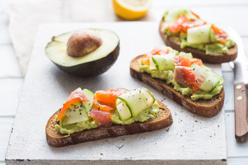 sandwich with avocado and salmon on a light background, green onions and gluten-free grain bread, radishes and tomatoes. concept diet food, copy space, sandwich take away, healthy fast food