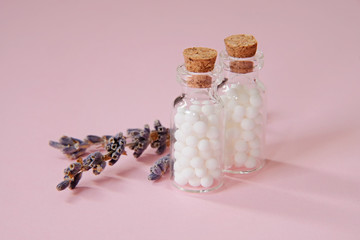 Homeopathic globules and glass bottle close up on pink background. Alternative Homeopathy medicine herbs, healthcare and pills concept. copyspace for text.