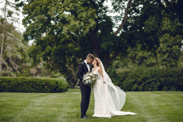 Beautiful bride in a long white dress. Handsome groom in a black suit. Couple in a summer park