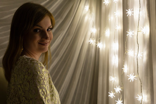 Portrait of a beautiful young white woman with brown hair in front of an illuminated star shaped christmas chain of lights