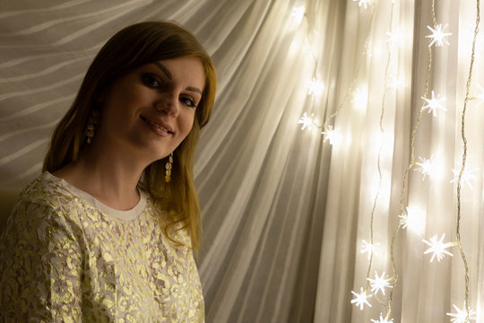Portrait of a beautiful young white woman with brown hair in front of an illuminated star shaped christmas chain of lights