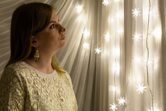 Portrait of a beautiful young white woman with brown hair in front of an illuminated star shaped christmas chain of lights