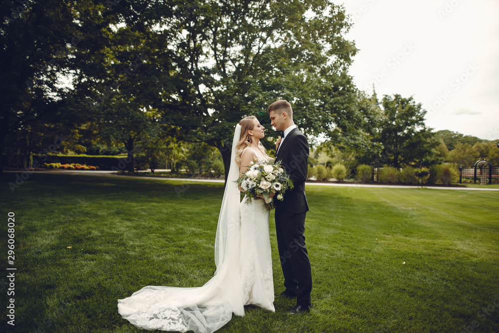 Wall mural beautiful bride in a long white dress. handsome groom in a black suit. couple in a summer park