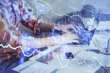 Double exposure of stock graph with businessman typing on computer in office on background. Concept of hard work.