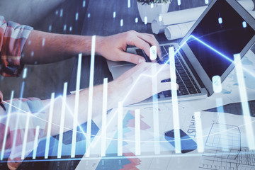 Double exposure of stock graph with businessman typing on computer in office on background. Concept...