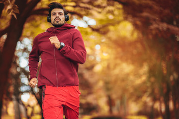 Young man running at park during autumn morning