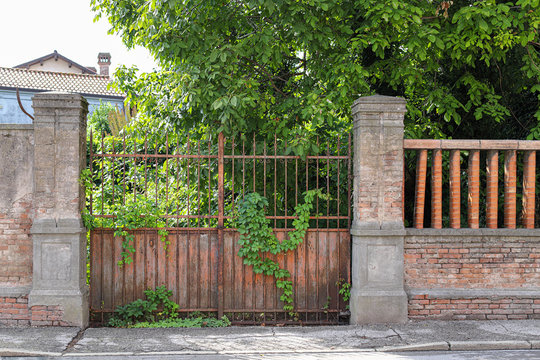 Gate of abandoned old house. Old rusty gate. Sidewalk near old house with garden overgrown with bushes