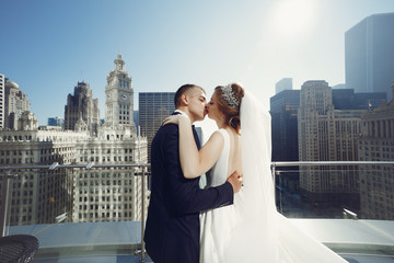 Elegant bride in a white dress and veil. Handsome groom in a blue suit. Couple in a big town
