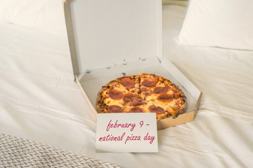 Open box of pizza on the big bed and card with text february 9 - national pizza day. Concept