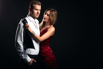 beautiful lady helping her serious husband to put on clothes , preparation for a party. going to work, close up portrait, isolated black background, studio shot, copy space , holiday