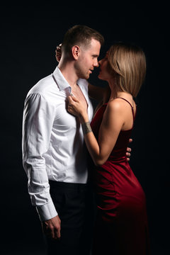 sexy woman holding the collar of her man's shirt and kissing him. close up photo. isolated black background, studio shot.