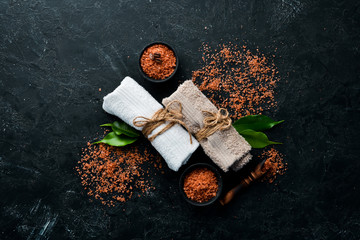 Brown Sea salt with towels. On a black stone background. Spa treatments. Top view. Free copy space.