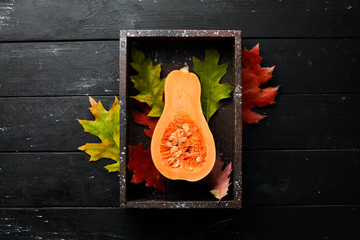 Fresh pumpkin in wooden box, autumn vegetables. On a black stone background. Top view. Free copy space.