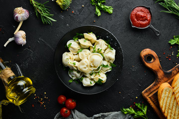 Russian pelmeni meat Dumplings with greens in a black plate. Russian traditional cuisine. Top view. Free copy space.