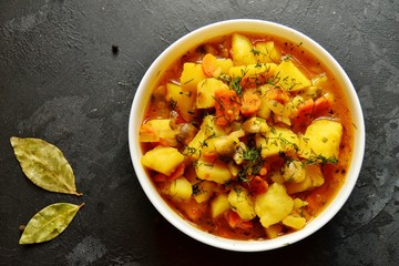Vegetable stew in a white bowl on a dark wooden background. A dish of potatoes. Appetizing hot food, with vegetables. Vegetable Vegetarian Stew. Bowl with potatoes on a wooden board for serving dishes