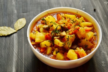 Vegetable stew in a white bowl on a dark wooden background. A dish of potatoes. Appetizing hot food, with vegetables. Vegetable Vegetarian Stew. Bowl with potatoes on a wooden board for serving dishes
