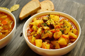 Vegetable stew in a white bowl on a dark wooden background. A dish of potatoes. Appetizing hot food, with vegetables. Vegetable Vegetarian Stew. Bowl with potatoes on a wooden board for serving dishes