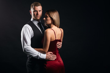portrait of a young fashion couple looking at each other while the man hugs woman, isolated black background. close up portrait, isolated black background, studio shot.copy space
