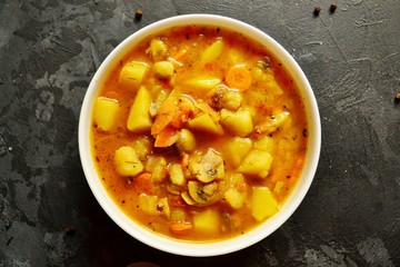 Vegetable stew in a white bowl on a dark wooden background. A dish of potatoes. Appetizing hot food, with vegetables. Vegetable Vegetarian Stew. Bowl with potatoes on a wooden board for serving dishes
