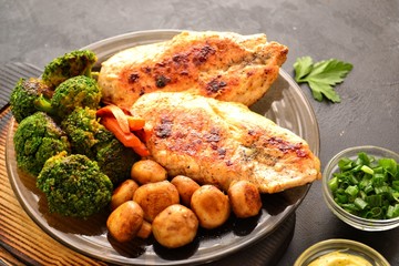Grilled chicken breast. Appetizing grilled chicken fillet. Meat with vegetables, broccoli and mushrooms. Food on a dark background. Chicken on the plate and wooden board