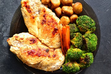Grilled chicken breast. Appetizing grilled chicken fillet. Meat with vegetables, broccoli and mushrooms. Food on a dark background. Chicken on the plate and wooden board