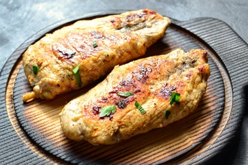 Grilled chicken breast. Chicken fillet with broccoli and mushrooms. Appetizing chicken meat on a wooden board on a dark background