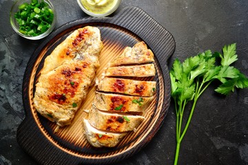 Grilled chicken breast. Chicken fillet with broccoli and mushrooms. Appetizing chicken meat on a wooden board on a dark background