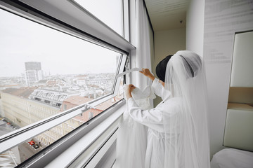 A elegant and beautiful bride at home standing near window