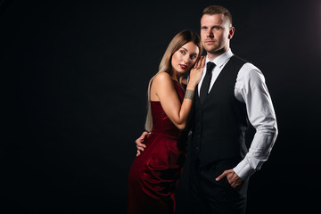 serious strong man in elegant clothes hugging his woman, protecting her. close up portrait, isolated black background, studio shot, strength, copy space