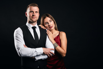 beautiful blonde woman leaning on her strong confident man with crossed arms, close up portrait, isolated black background, studio shot
