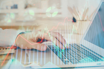 Double exposure of man's hands writing notes with laptop of stock market with forex graph...