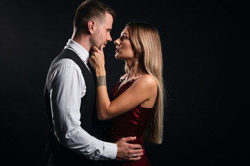 blonde attractive woman looking at her boyfriend, touching his chin, telling him secret, close up side view photo. isolated black background, warm , tender feeling